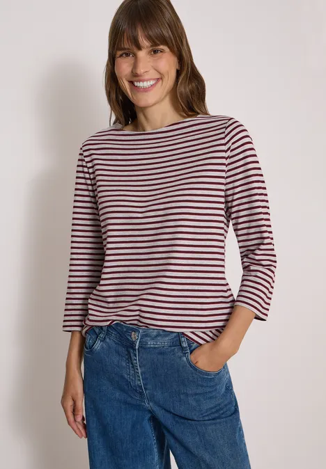 3/4-Arm Shirt mit Boat Neck und Streifen light grey melange Frau lächelt in gestreiftem Langarmshirt und blauen Jeans, Hand in der Hosentasche vor neutralem Hintergrund.