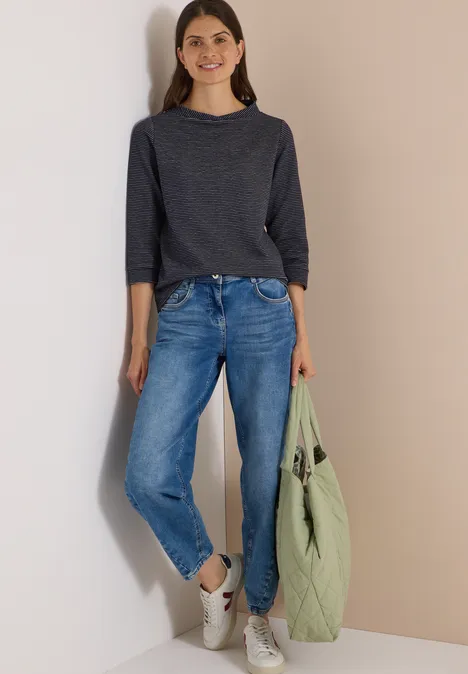 Ottoman Shirt im Two-Tone-Look urban dark blue Frau in dunkelgrauem Langarmshirt, blauen Jeans und weißen Sneakern, hält eine hellgrüne Tasche.