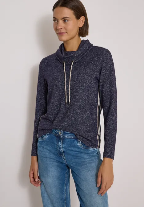 T-shirt souple à col et bande de renfort urban dark blue melange Frau trägt lässigen dunkelblauen Pullover mit Kordelzug und Jeans vor hellem Hintergrund.