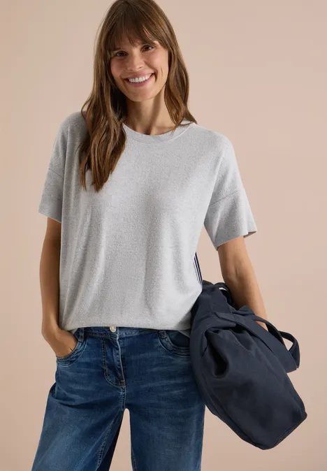 Shirt met aflopende schouders, ronde hals en band light grey melange Eine lächelnde Frau in grauem T-Shirt und Jeans trägt eine dunkelblaue Tasche vor hellem Hintergrund.