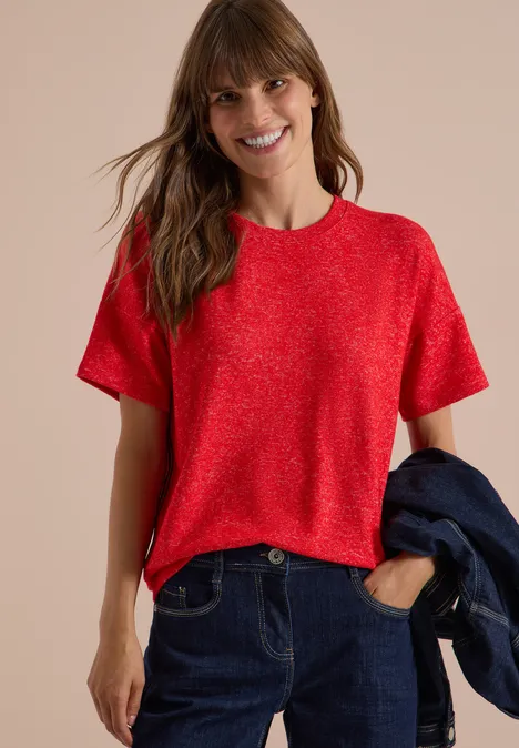 Shirt met verlaagde schouders, ronde hals en band flame red melange Frau trägt rotes T-Shirt, Jeans, hält Jeansjacke und lächelt.