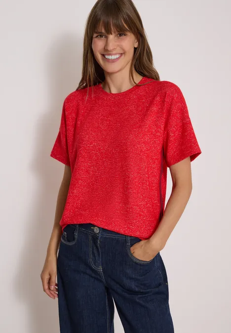 Shirt met verlaagde schouders, ronde hals en band flame red melange Lächelnde Frau in rotem Kurzarmshirt und blauer Jeans, eine Hand in der Hosentasche.