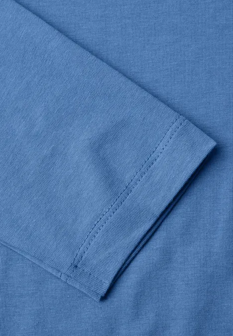 Gros plan d’un t-shirt bleu plié, mettant en évidence la couture de la manche.
