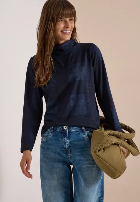 T-shirt à manches longues, col roulé et imprimé urban dark blue Femme en pull col montant bleu foncé et jean, souriante, tenant un sac olive noué.