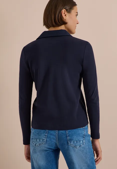 Frau von hinten in dunkelblauem Blazer und Jeans, schulterlanges Haar.