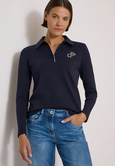 Frau trägt dunkelblauen Langarm-Pullover mit Reißverschluss und Jeans, Hand in Tasche.