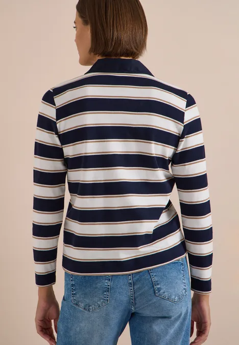 Rückansicht einer Person mit gestreiftem Langarm-Poloshirt (marine-weiß) und blauen Jeans vor beigem Hintergrund.