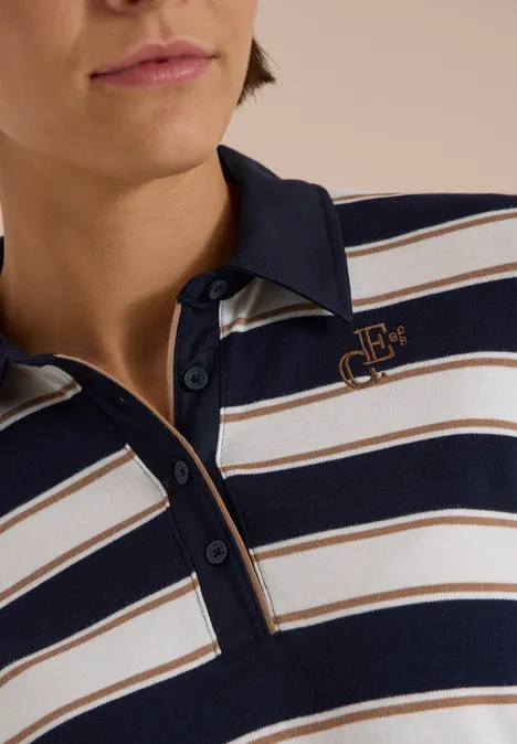 Person trägt ein gestreiftes Poloshirt in Marineblau, Weiß und Beige mit einem Logo auf der Brust.