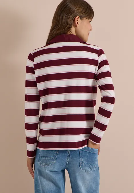 Langarm Poloshirt mit Knöpfen red wine Frau von hinten in rot-weiß gestreiftem Pullover und blauen Jeans vor beigem Hintergrund.