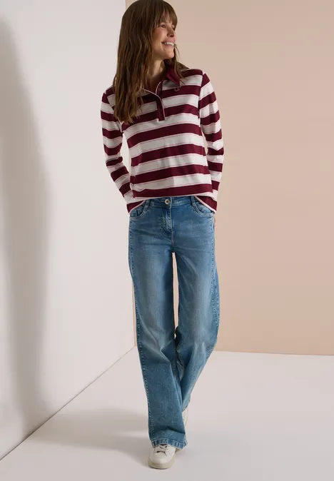 Langarm Poloshirt mit Knöpfen red wine Frau in gestreiftem Pullover und weiten Jeans steht lässig vor neutralem Hintergrund.