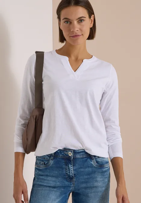 Frau in weißem Langarmshirt und Jeans, trägt eine Tasche über der Schulter.