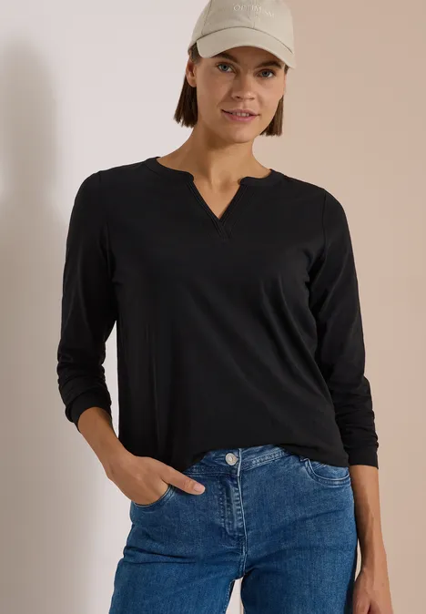 Langarm Shirt im Tunika-Look Black Frau in schwarzem Langarmshirt, blauen Jeans und Baseball-Cap lehnt entspannt mit einer Hand in der Hosentasche.