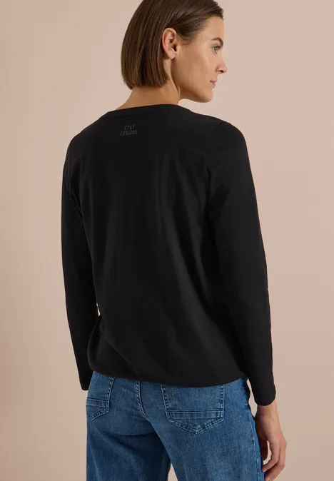 Langarm Shirt im Tunika-Look Black Eine Frau von hinten in schwarzem Pullover und blauen Jeans vor beigem Hintergrund.