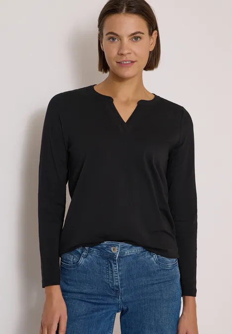 Langarm Shirt im Tunika-Look Black Frau in schwarzem Langarmshirt mit V-Ausschnitt, lässig in blaue Jeans gesteckt, vor hellem Hintergrund.