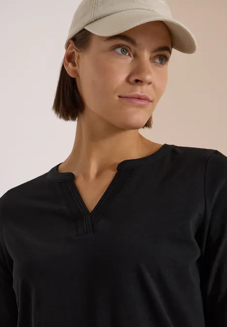 Langarm Shirt im Tunika-Look Black Eine Frau in schwarzem V-Neck-Oberteil und beiger Baseballmütze blickt seitlich.