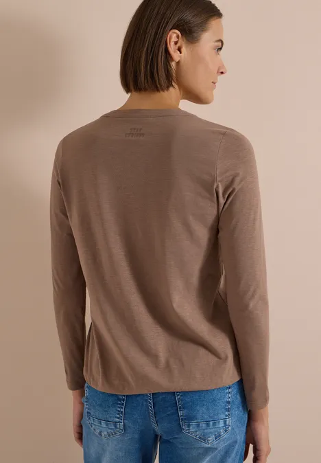Eine Frau von hinten, trägt ein taupefarbenes Langarmshirt und blaue Jeans.
