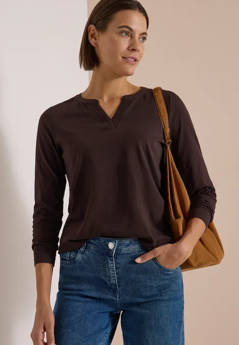 Langarm Shirt im Tunika-Look truffle brown Dame mit braunem Langarmshirt, blauen Jeans und Schultertasche vor neutralem Hintergrund.