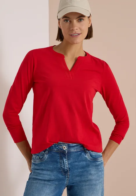 Langarm Shirt im Tunika-Look flame red Frau in rotem langärmligem Shirt, blauen Jeans und weißer Cap, steht vor hellem Hintergrund.