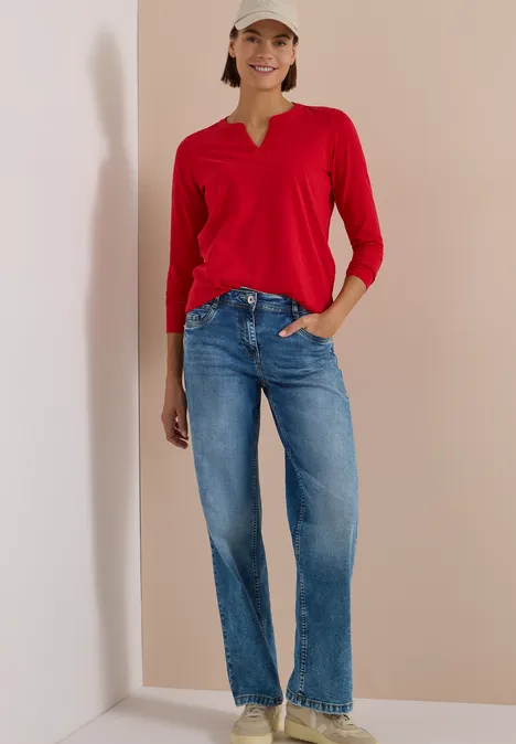Langarm Shirt im Tunika-Look flame red Frau in rotem Langarmshirt und blauen Jeans steht vor schlichtem Hintergrund und lächelt.
