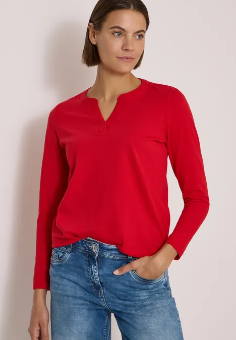 Langarm Shirt im Tunika-Look flame red Eine Frau in rotem Langarmshirt und blauen Jeans steht vor hellem Hintergrund, eine Hand in der Hosentasche.