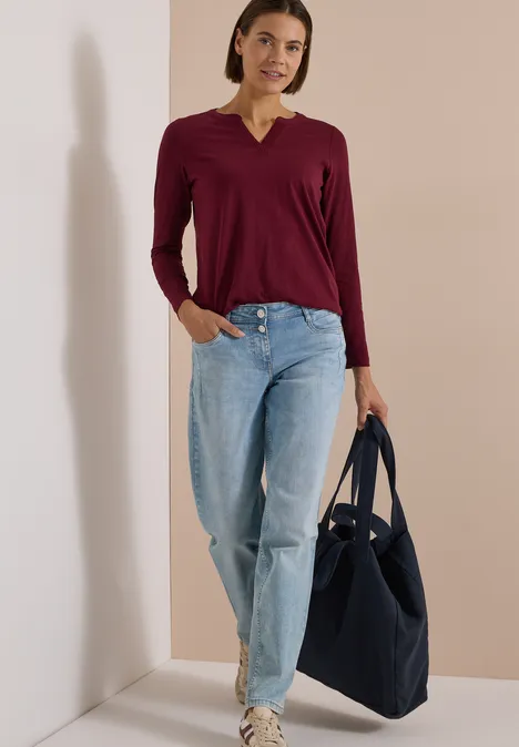 Langarm Shirt im Tunika-Look red wine Frau in Bordo-Shirt und blauen Jeans steht mit dunkelblauer Tasche vor hellem Hintergrund und lächelt.