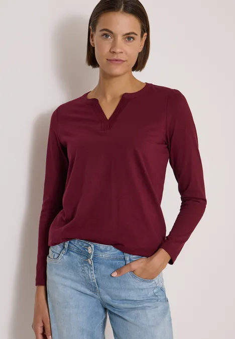 Langarm Shirt im Tunika-Look red wine Frau mit bordeauxrotem Langarmshirt und hellblauen Jeans, lässig mit einer Hand in der Tasche stehend.