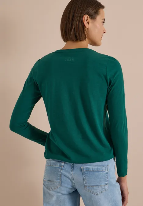 Langarm Shirt im Tunika-Look dark fir green Eine Frau steht in grünem Langarmpullover und Jeans vor neutralem Hintergrund, Rückenansicht.