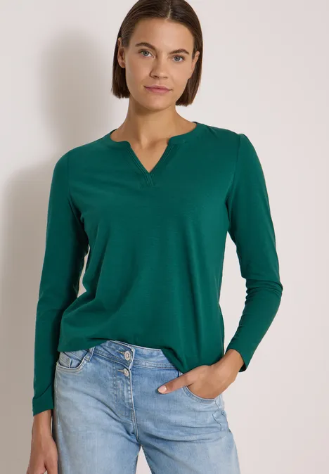 Langarm Shirt im Tunika-Look dark fir green Eine Frau trägt ein grünes Langarmshirt und blaue Jeans, steht vor neutralem Hintergrund.