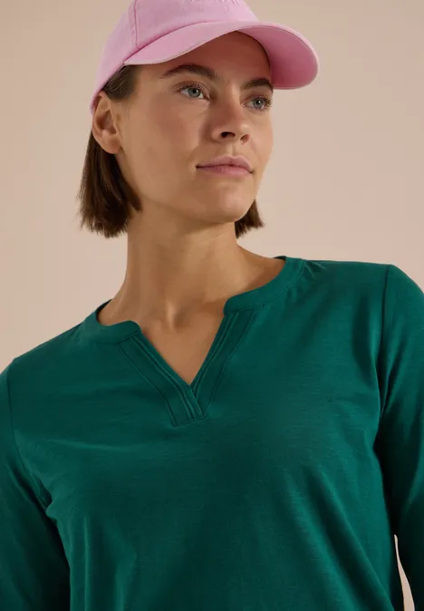 Langarm Shirt im Tunika-Look dark fir green Eine Frau mit kurzem braunen Haar trägt ein grünes Shirt und eine rosa Baseballkappe, Blick seitlich.