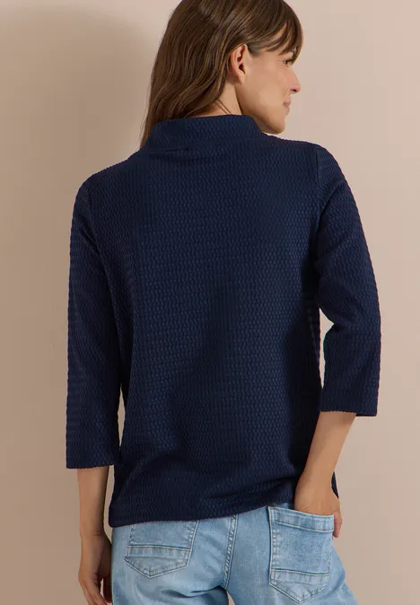 Frau von hinten in dunkelblauem, texturiertem Dreiviertelärmel-Pullover und hellen Jeans.