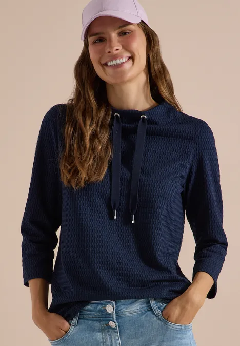 Fröhliche Frau mit dunkelblauem Kapuzenpullover, Jeans und rosa Baseballcap.