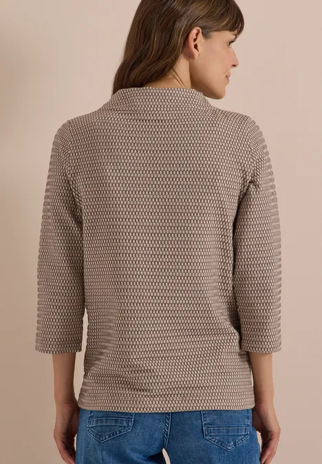 T-shirt à manches 3/4, col cheminée et texture urban taupe Femme de dos portant un pull gaufré beige à manches 3/4 et un jean bleu.