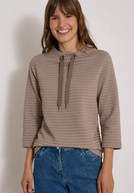 T-shirt à manches 3/4, col cheminée et texture urban taupe Femme souriante en sweat à capuche beige texturé et jean, sur fond clair.