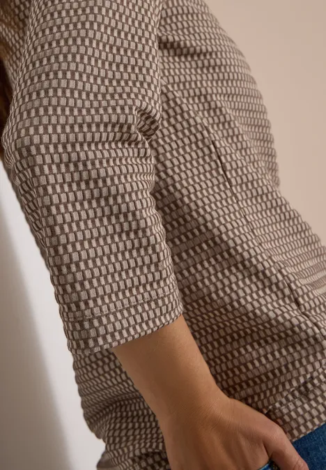 T-shirt à manches 3/4, col cheminée et texture urban taupe Gros plan d’une personne portant un haut à motif géométrique, manches 3/4, main posée sur la hanche.