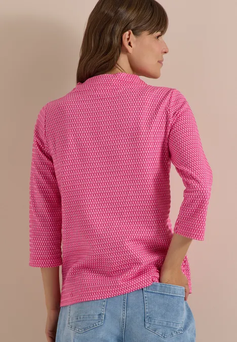T-shirt à manches 3/4, col cheminée et texture pink flash Vue de dos d'une femme portant un jean et un t-shirt 3/4 rose à motif sur fond neutre
