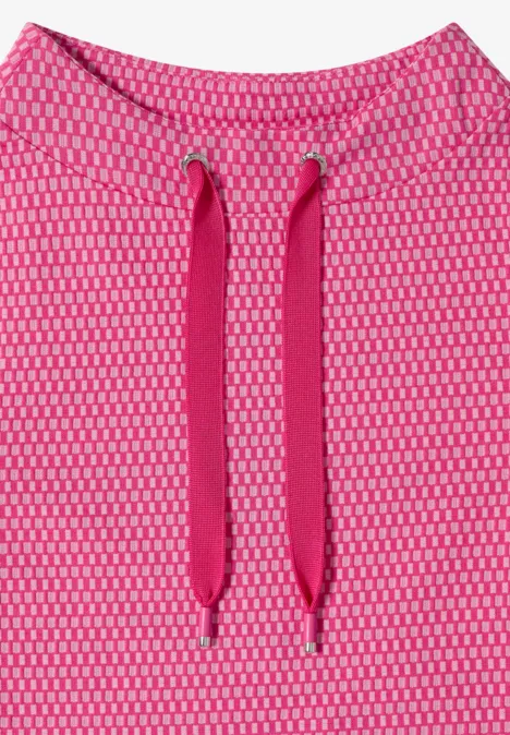 T-shirt à manches 3/4, col cheminée et texture pink flash Gros plan d’un tissu rose ajouré avec deux cordons de capuche.