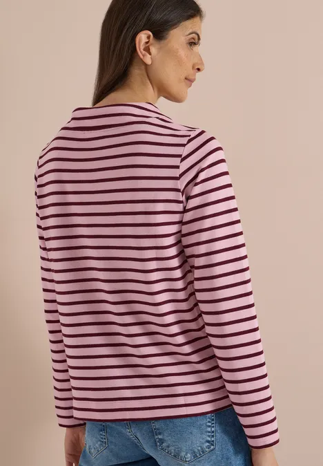 Een vrouw gezien van achteren draagt een roze T-shirt met zwarte strepen en een blauwe spijkerbroek.