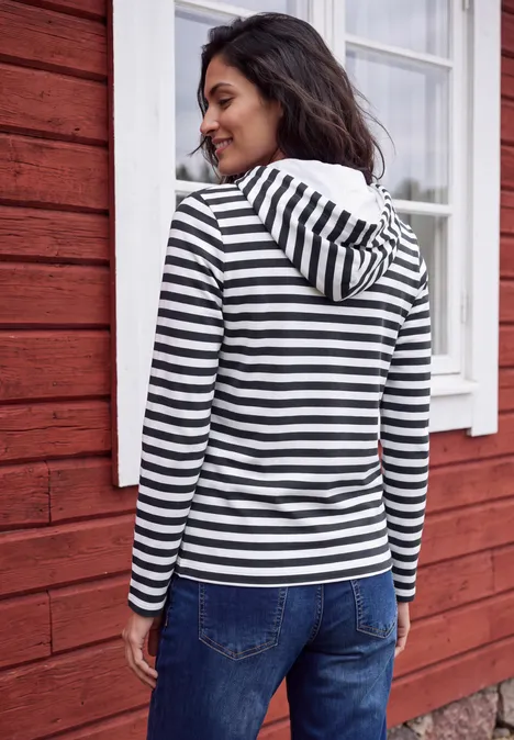 Shirt met lange mouwen, capuchon en strepen urban dark blue Frau in einem schwarz-weißen Kapuzenpullover lehnt vor einem roten Haus