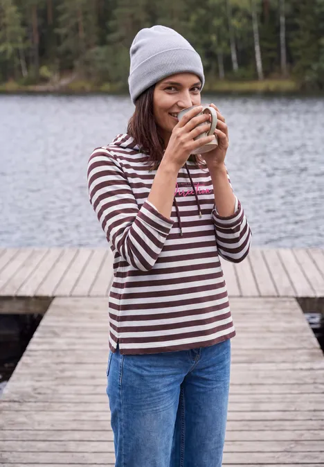 Shirt met lange mouwen, capuchon en strepen red wine Junge Frau in gestreiftem Pullover steht auf einem Steg am See und trinkt lächelnd aus einer Tasse.