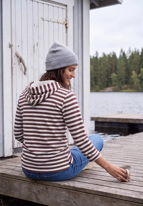 Shirt met lange mouwen, capuchon en strepen red wine Person in gestreiftem Hoodie und Mütze sitzt auf Holzsteg am See, hält eine Tasse, Wald im Hintergrund.