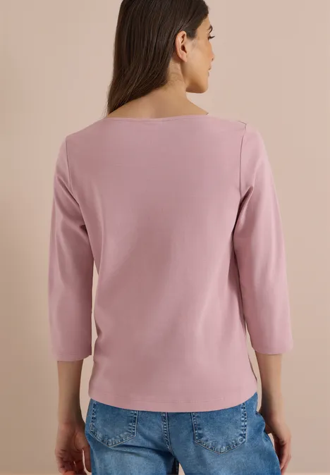 Frau von hinten in rosa 3/4-Arm-Shirt und blauen Jeans vor hellem Hintergrund