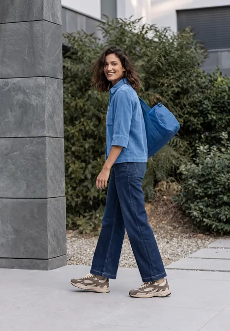 Une jeune femme en jean et baskets avec un sac à dos bleu marche tranquillement sur le trottoir.