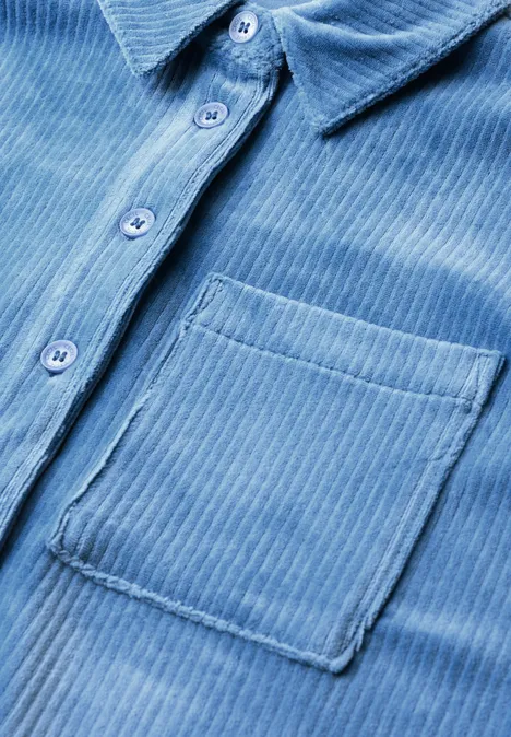 Gros plan sur une chemise en velours côtelé bleu clair avec patte de boutonnage et poche.