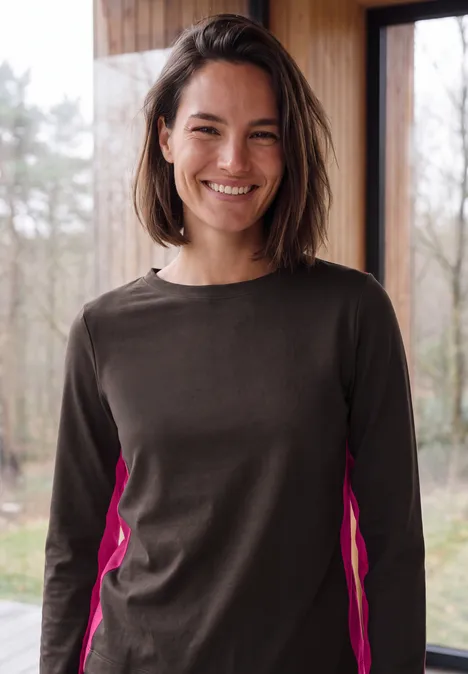 Femme souriante en pull marron avec empiècements roses sur fond lumineux.