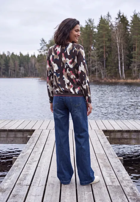 T-shirt à manches longues, col bateau et imprimé pink flash Frau steht im Camouflage-Pullover und weiter Jeans mit dem Rücken zur Kamera auf einem Steg am See.