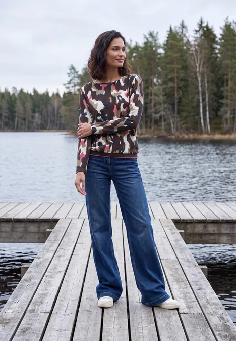 T-shirt à manches longues, col bateau et imprimé pink flash Eine Frau in Camouflage-Pullover und weiten Jeans steht auf einem Holzsteg an einem Waldsee.