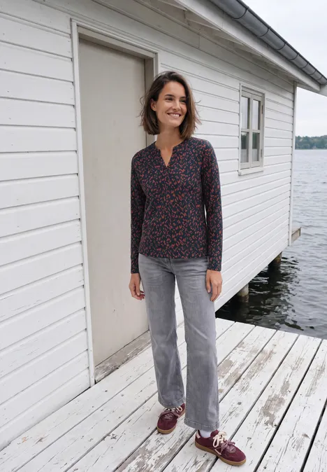 Shirt mit Split Neck im Tunika-Look urban dark blue Eine Frau steht auf einem Holzsteg vor einem weißen Bootshaus am See.