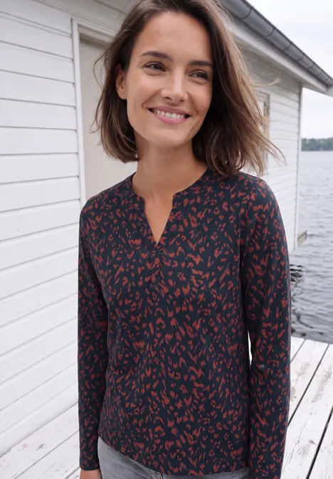 Shirt mit Split Neck im Tunika-Look urban dark blue Eine lächelnde Frau mit schulterlangen braunen Haaren trägt eine dunkelblau-rote Bluse und steht auf einem Steg am Wasser.