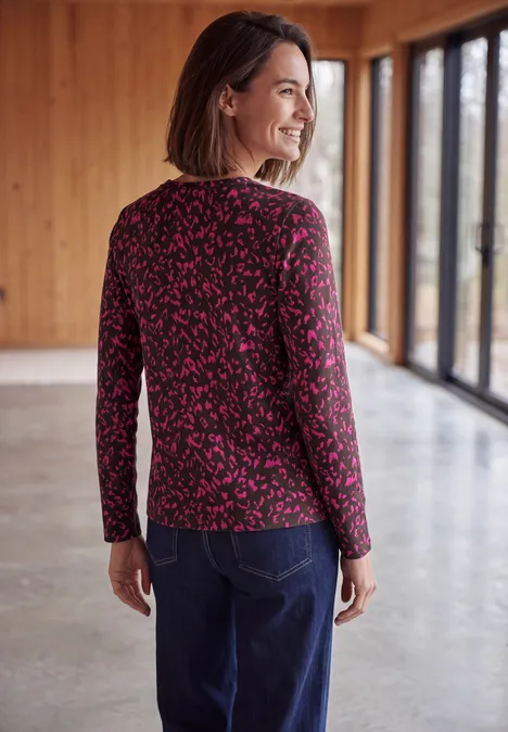 Shirt met split in de hals, in tuniekstijl truffle brown Vrouw met de rug naar de camera in lichte houten ruimte, draagt een roze-zwart shirt met lange mouwen en blauwe jeans.