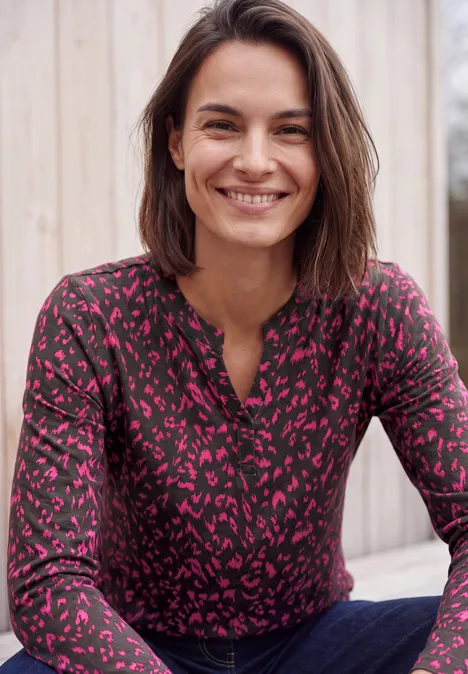 Shirt met split in de hals, in tuniekstijl truffle brown Glimlachende vrouw met bruin haar draagt een zwart-roze top met print voor een houten wand.